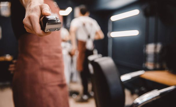 Barber holds hair clipper in modern barbershop for men, brown retro - Valokuva, kuva