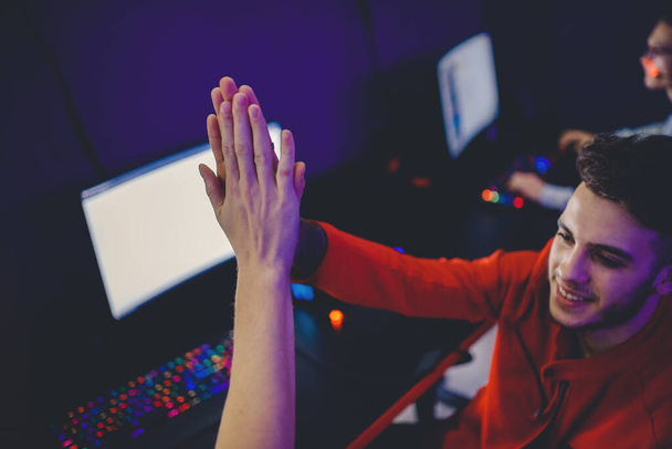 Professzionális játékos üdvözlő és támogató csapat öklök kezek online játék neon szín elmosódott háttér. Lágy fókusz, visszapillantás - Fotó, kép