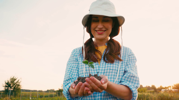 brunette vrouw in hoed houden terrein met kleine plant in handen - Video