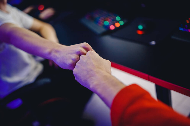 Professional gamer greeting and support team fists hands online game in neon color blur background. Soft focus, back view - Foto, immagini