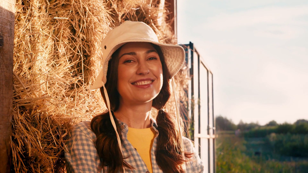 woman in hat leaning on hay stack and looking at camera - Materiał filmowy, wideo