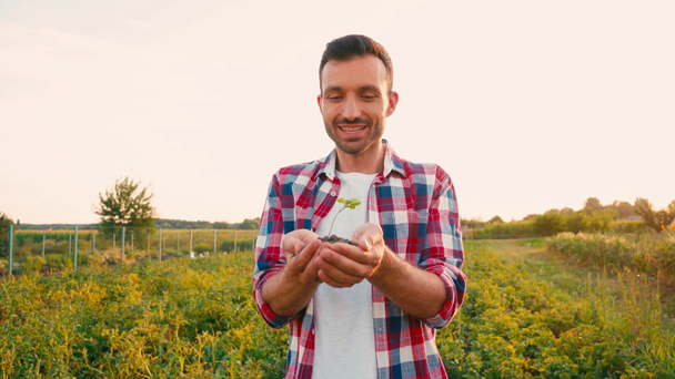 vzrušený vousatý muž mluví a drží půdu s malou rostlinou v rukou - Záběry, video