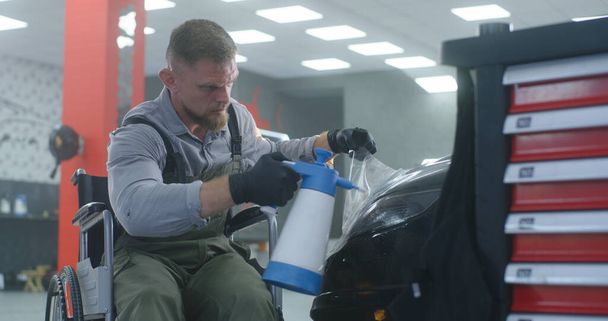 Mechanic on wheelchair applying film on car headlight - Photo, Image