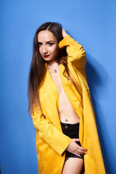 Güzel bir kız mavi bir duvara karşı sarı bir ceketle poz veriyor.                  - Fotoğraf, Görsel