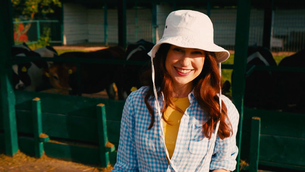 brunetka kobieta w kapeluszu wskazując z ręki na krowy w pobliżu ogrodzenia  - Materiał filmowy, wideo