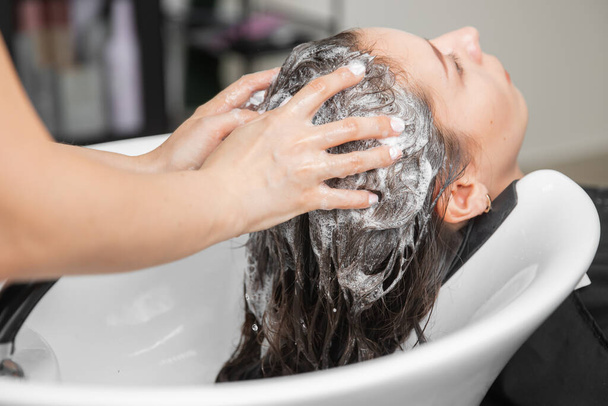 Шампунь волос в салоне красоты юной брюнетки, парикмахерская забота о клиенте - Фото, изображение
