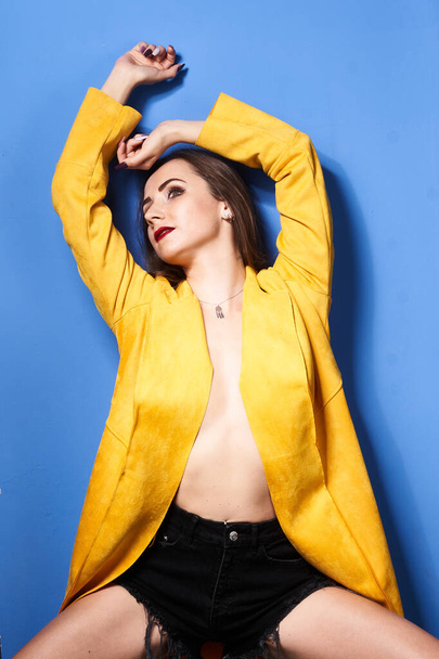  a beautiful girl poses in a yellow coat against a blue wall            - Photo, Image