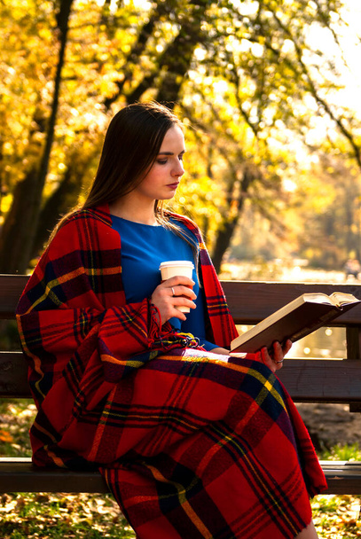 Молода дівчина з книгою і кавою в осінньому парку
 - Фото, зображення