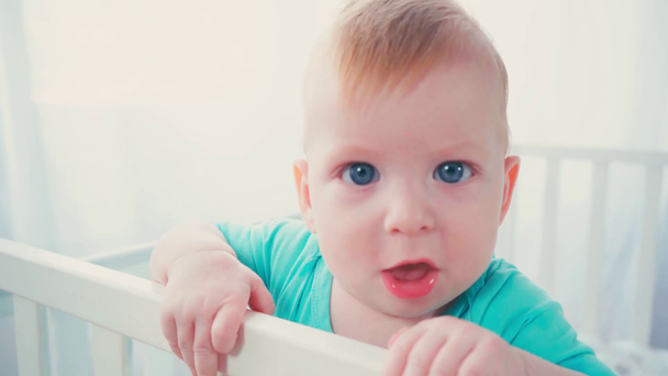 pikkupoika seisoo vauvansängyssä ja katselee kameraa  - Materiaali, video