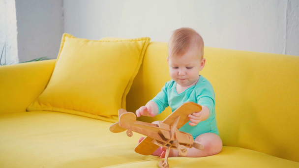 baby jongen zitten op de bank en spelen met houten tweedekker - Video