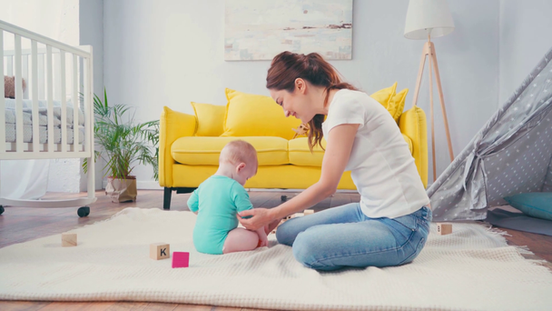 Mutter sitzt auf dem Boden und spielt mit Säugling im Wohnzimmer  - Filmmaterial, Video