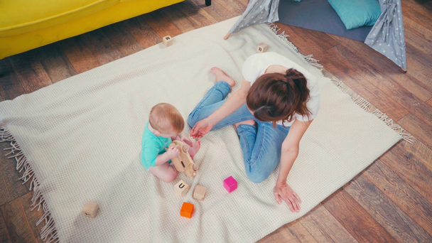 κορυφαία άποψη της ξυπόλητης μητέρας κάθεται κοντά στο παιδί γιο παίζει με τα παιχνίδια  - Πλάνα, βίντεο