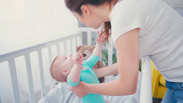 брюнетка женщина трогает и разговаривает с младенцем в кроватке  - Кадры, видео