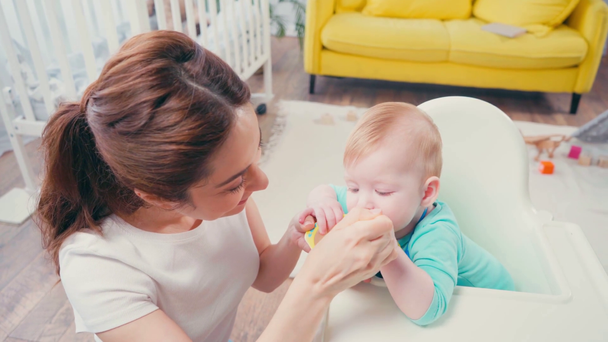 high angle view of brunette mother feeding infant son with baby food - Footage, Video