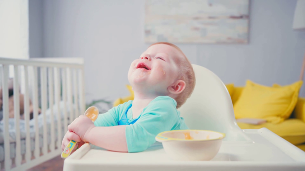 pikkulapsi poika imee lusikka vauvanruokaa lähellä kulho pöydällä  - Materiaali, video