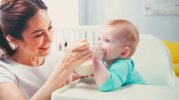 брюнетка женщина кормит возбужденного младенца с детским питанием - Кадры, видео