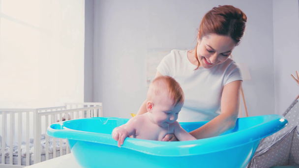 madre tocando mojado bebé hijo tomando baño en bebé bañera  - Metraje, vídeo