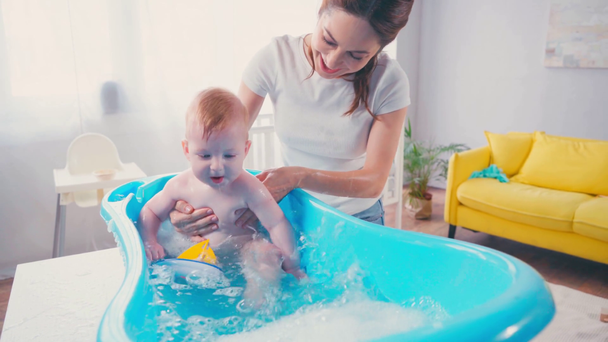 μητέρα αγγίζοντας το βρέφος γιος παίζει με το παιχνίδι, ενώ λαμβάνοντας μπάνιο σε μπανιέρα μωρό  - Πλάνα, βίντεο