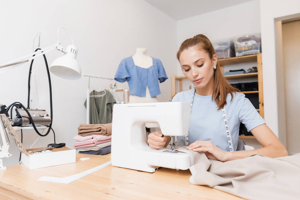 Ευτυχισμένη γυναίκα ράφτης ράφτης λειτουργεί με την προσαρμογή νέα και μοντέρνα ρούχα, ράψτε το χώρο εργασίας - Φωτογραφία, εικόνα