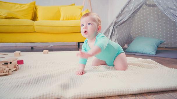 baby boy looking at camera while crawling on blanket near sofa and tent  - Footage, Video