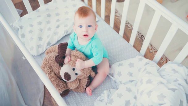 Bebek karyolasında oyuncak ayıyla oynayan çıplak ayaklı çocuk manzarası.  - Video, Çekim