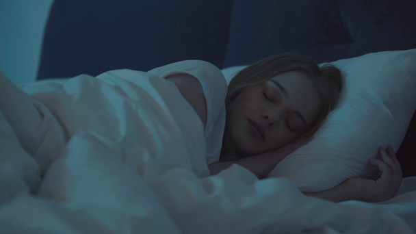 jonge vrouw liggend in bed en slapen 's nachts - Video