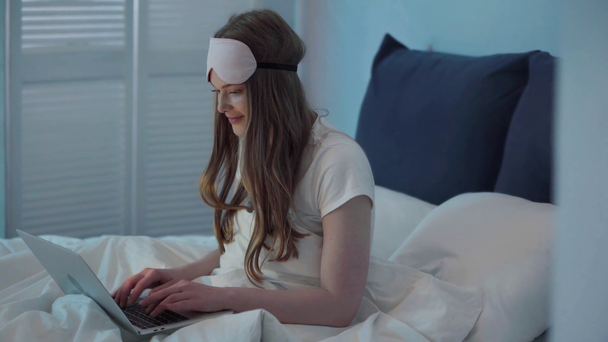 Giovane donna digitando sul computer portatile e seduto sul letto - Filmati, video