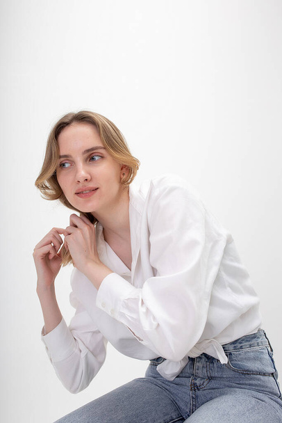 młody słodkie uśmiech biały dziewczyna pozowanie w biały koszula niebieski dżinsy w studio - Zdjęcie, obraz