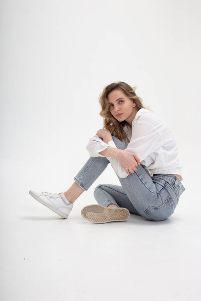 caucasian woman posing in shirt and blue jeans, sitting on white studio floor - Fotoğraf, Görsel
