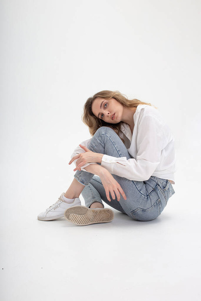 caucasian woman posing in shirt and blue jeans, sitting on white studio floor - Foto, immagini