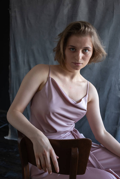 caucasian young woman with short hair in pink suit sitting on chair in studio - Photo, Image