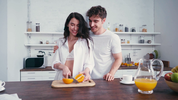 Homem beijando mulher em sutiã e camisa durante o café da manhã na cozinha  - Filmagem, Vídeo