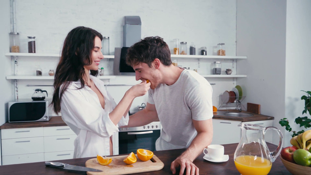 Seksikäs nainen ruokinta poikaystävä tuoretta oranssi keittiössä  - Materiaali, video