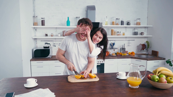 Sexy woman covering eyes to boyfriend cutting orange during breakfast - Video, Çekim