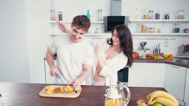Mulher sexy cobrindo olhos para namorado cortando laranja durante o café da manhã  - Filmagem, Vídeo