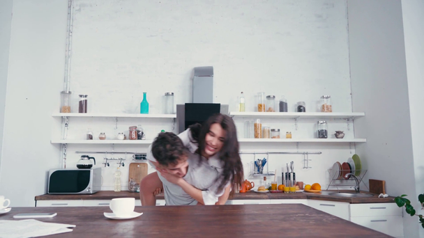 Mujer en lencería y camisa piggybacking en novio cerca de café en la mesa  - Imágenes, Vídeo