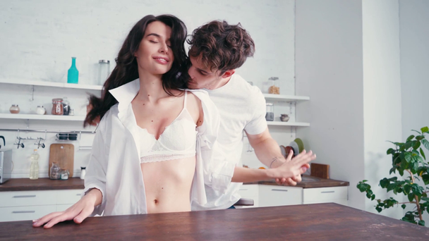 Uomo toccando fidanzata sexy in reggiseno e camicia in cucina  - Filmati, video