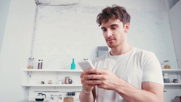 Nuori mies, joka käyttää älypuhelinta keittiössä kotona - Materiaali, video