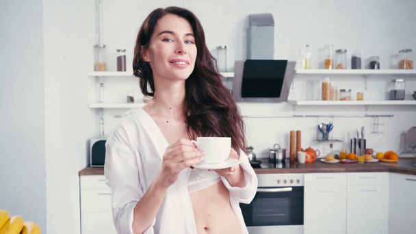 Женщина в лифчике и рубашке пьет кофе на кухне  - Кадры, видео