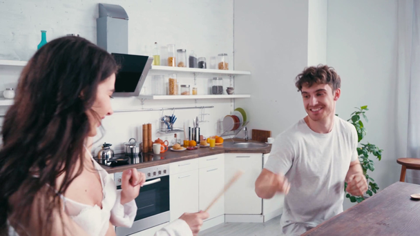 Mann mit Spachtel kämpft mit sexy Frau in BH und Hemd in Küche  - Filmmaterial, Video