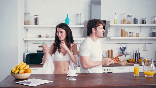 Sexy pareja bailando cerca de café y naranja en la mesa de la cocina  - Imágenes, Vídeo