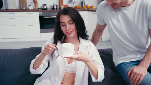 Mann gibt Kaffee an sexy Frau auf Sofa zu Hause  - Filmmaterial, Video