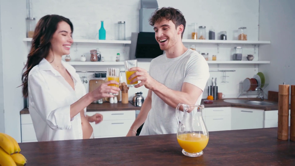 Hombre abrazando sexy novia mientras bebe jugo de naranja en la cocina  - Metraje, vídeo