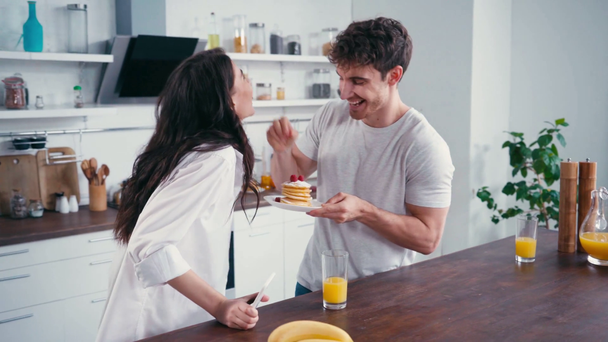 man met pannenkoeken voeden sensuele vrouw met smartphone in keuken  - Video