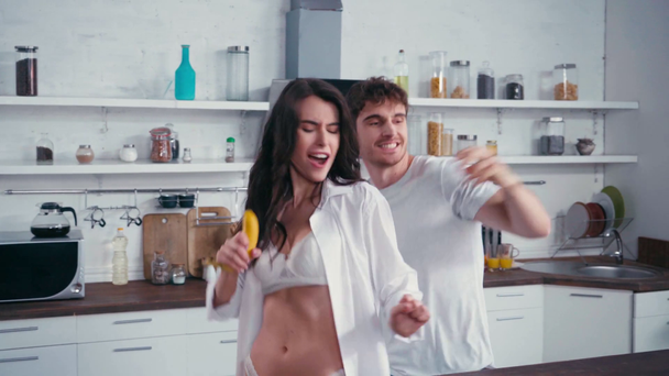 Сексуальная женщина танцует рядом с парнем, фрукты и смартфон на кухонном столе  - Кадры, видео