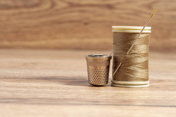A roll of brown thread with a needle and a thimble - Foto, Bild