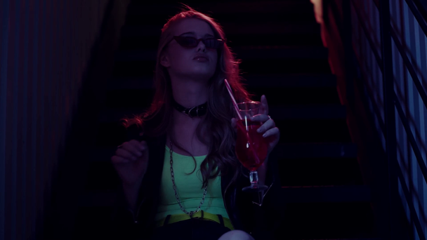 Nainen aurinkolasit juominen cocktail ja istuu portaissa - Materiaali, video