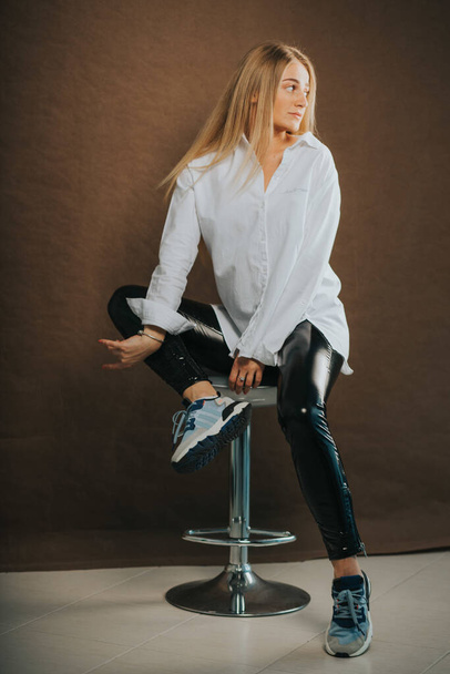 A vertical shot of an attractive blonde female posing while sitting on a barstool - Foto, afbeelding