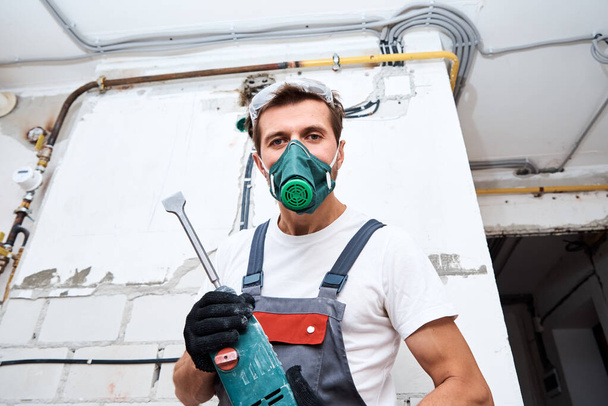 Man in bouwvakker uniform met hamer boor reparaties in de kamer. Renovatieconcept - Foto, afbeelding