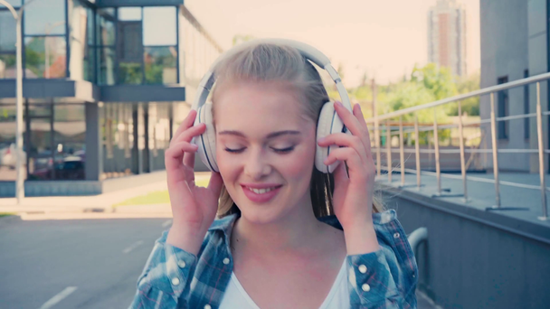 jovem mulher usando fones de ouvido sem fio e andando fora - Filmagem, Vídeo